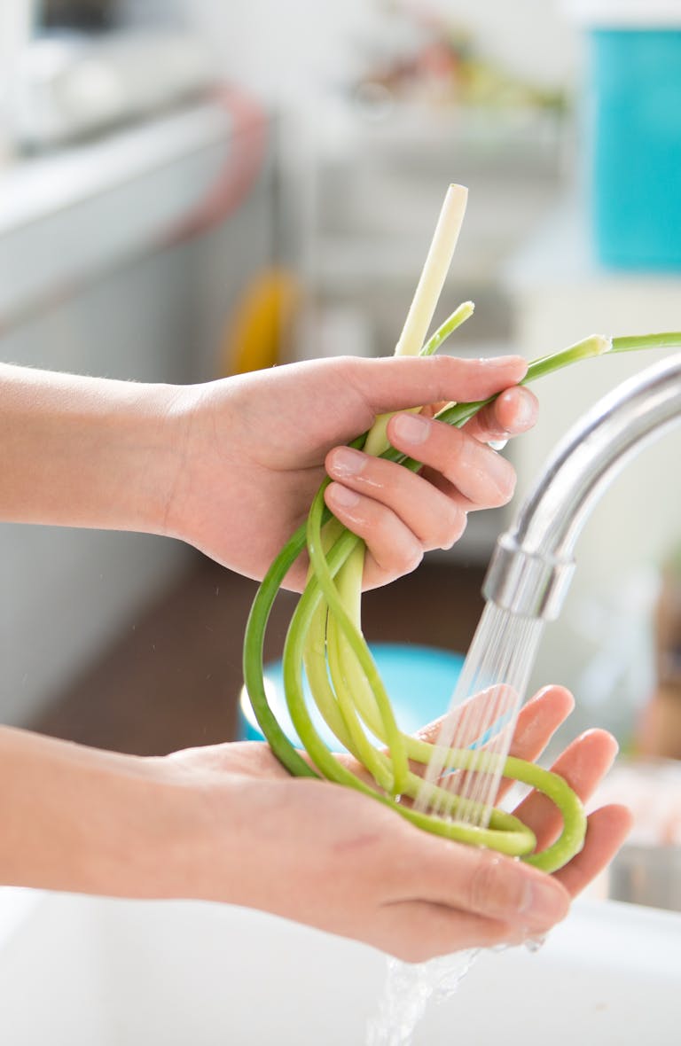 Close-up of hands washing green vegetables under a best kitchen sink faucet for cleanliness.